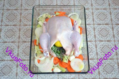 Курицу уложить на овощи. Внутрь курицы положить травы и лимон.